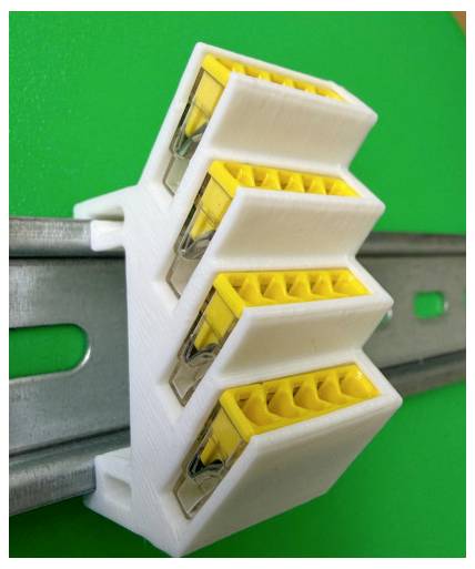 Staffa bianca stampata in 3D che tiene quattro moduli di connettori gialli attaccati a una guida in metallo grigio su uno sfondo verde.