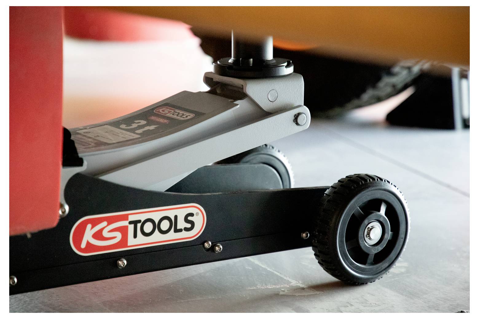 Primo piano di una ruota di cric da pavimento e braccio con logo KS Tools, che supporta un veicolo o attrezzatura in un'officina.