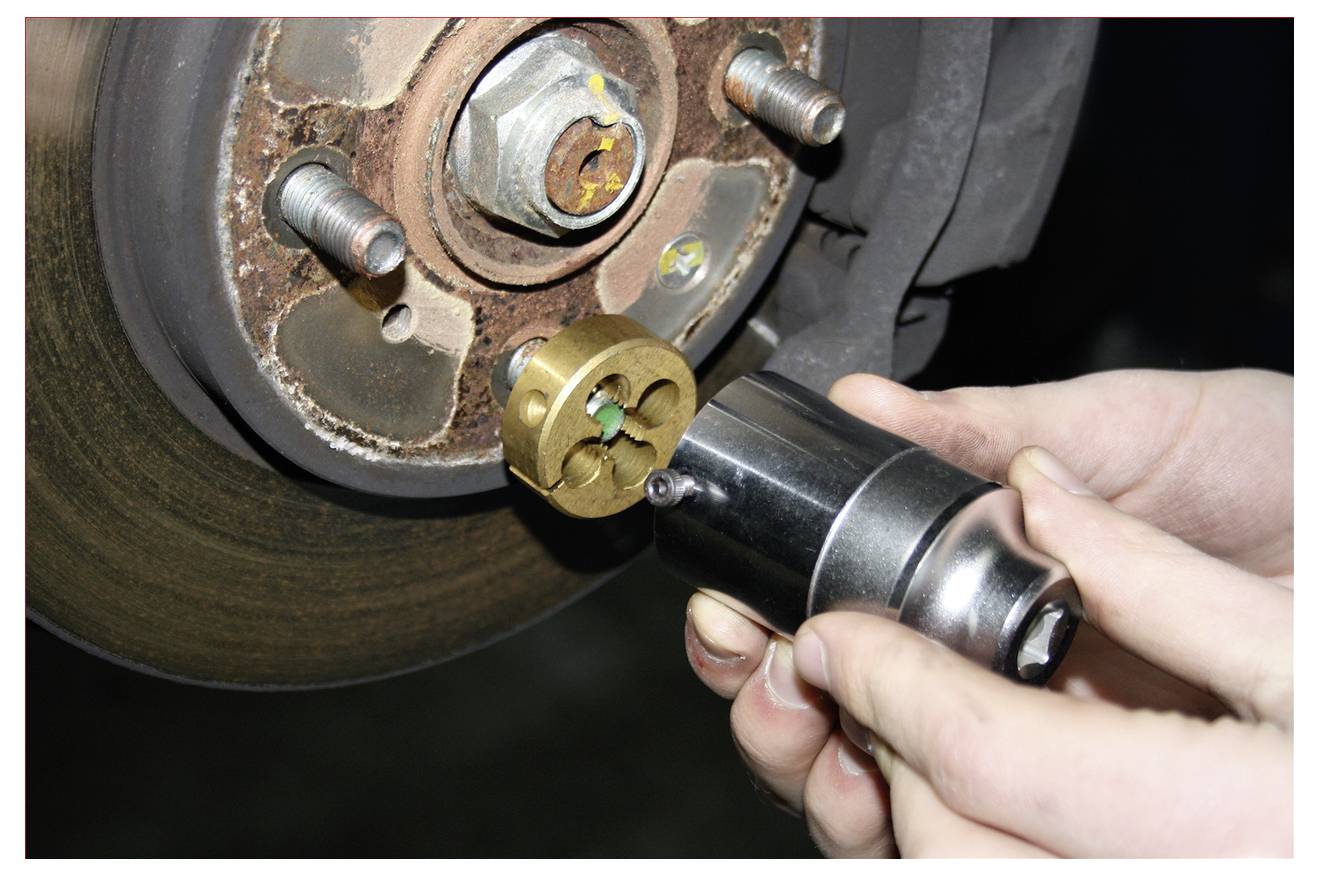 Primo piano di un meccanico che utilizza un attrezzo manuale per rimuovere o installare un dado della ruota su un mozzo di freno a disco di un'auto.
