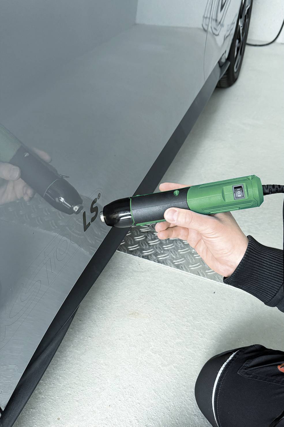 Una persona utilizza uno strumento di ispezione elettrico verde su un pannello porta di un'auto, probabilmente per verificare i difetti di superficie o i danni.