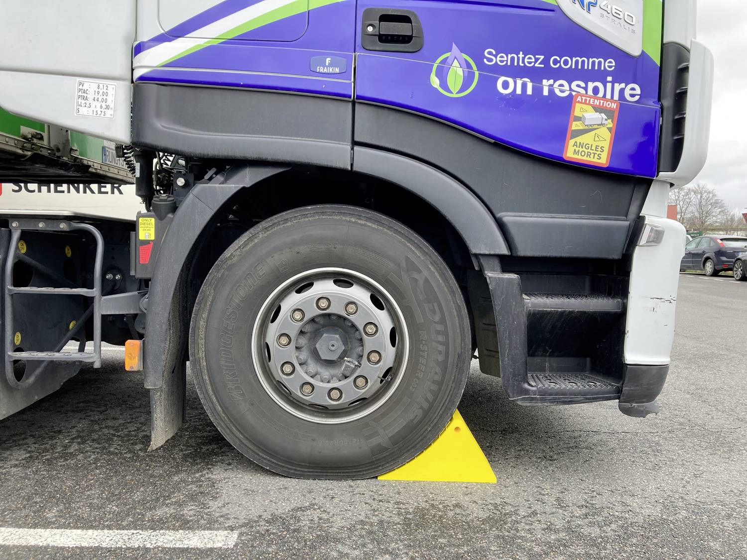 Vista laterale di una cabina di camion con la ruota anteriore ferma su una rampa triangolare gialla per il parcheggio o uno stopper di ruota in un parcheggio.