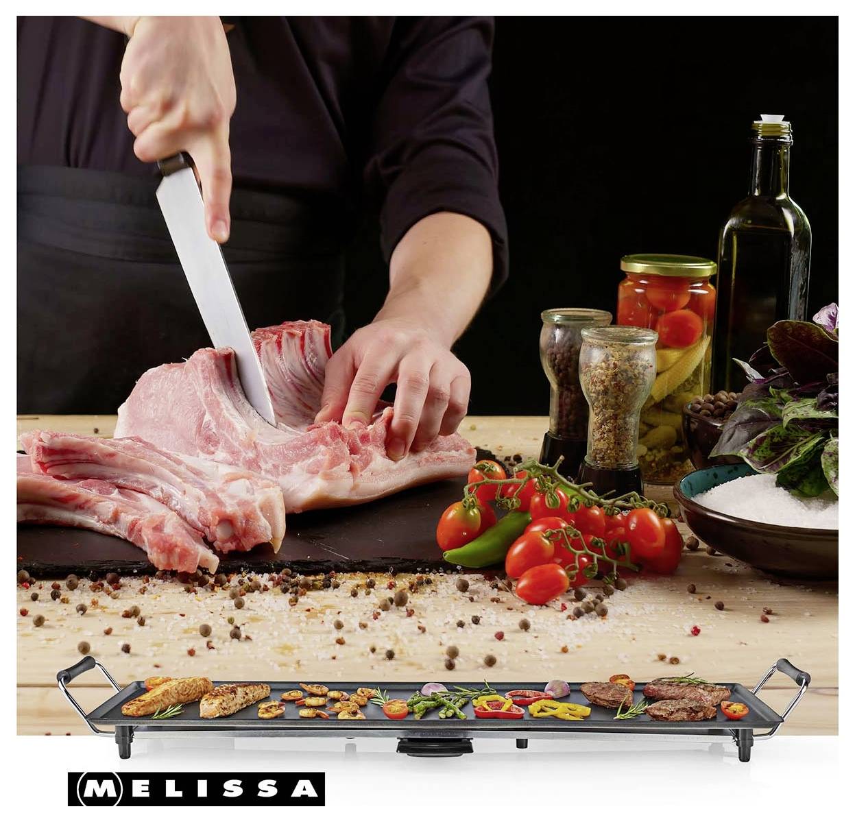 Persona che affetta carne cruda su un tagliere accanto a spezie, verdure e olio da cucina, con un grill da tavolo Melissa esposto di seguito.