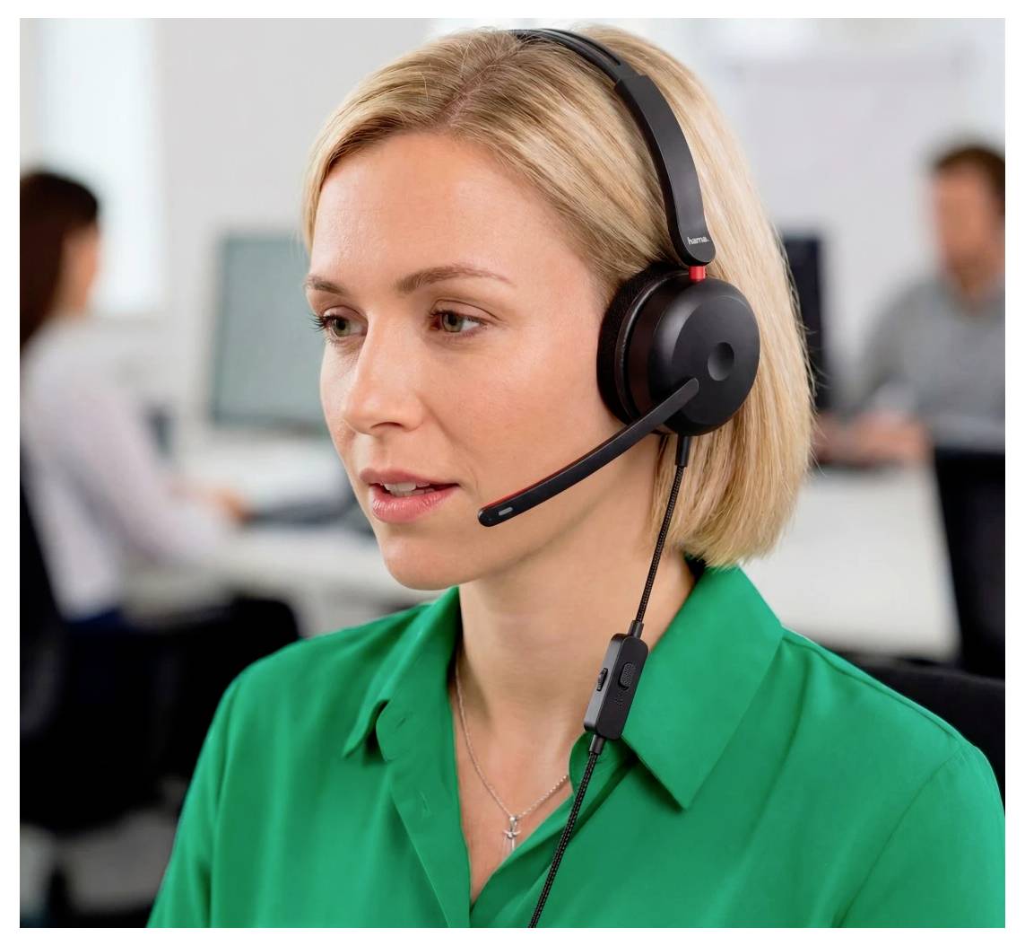 Donna in una camicia verde che indossa un auricolare con microfono, che lavora in un call center con colleghi sfocati sullo sfondo.