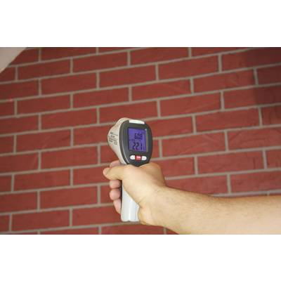Una mano tiene un termometro a infrarossi davanti a un muro di mattoni rossi, mostrando una temperatura di 22,1 gradi Celsius.