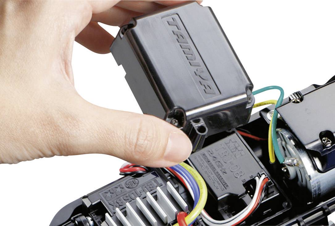 Una mano solleva un coperchio nero e rettangolare in plastica da un dispositivo elettrico con fili e connettori visibili.