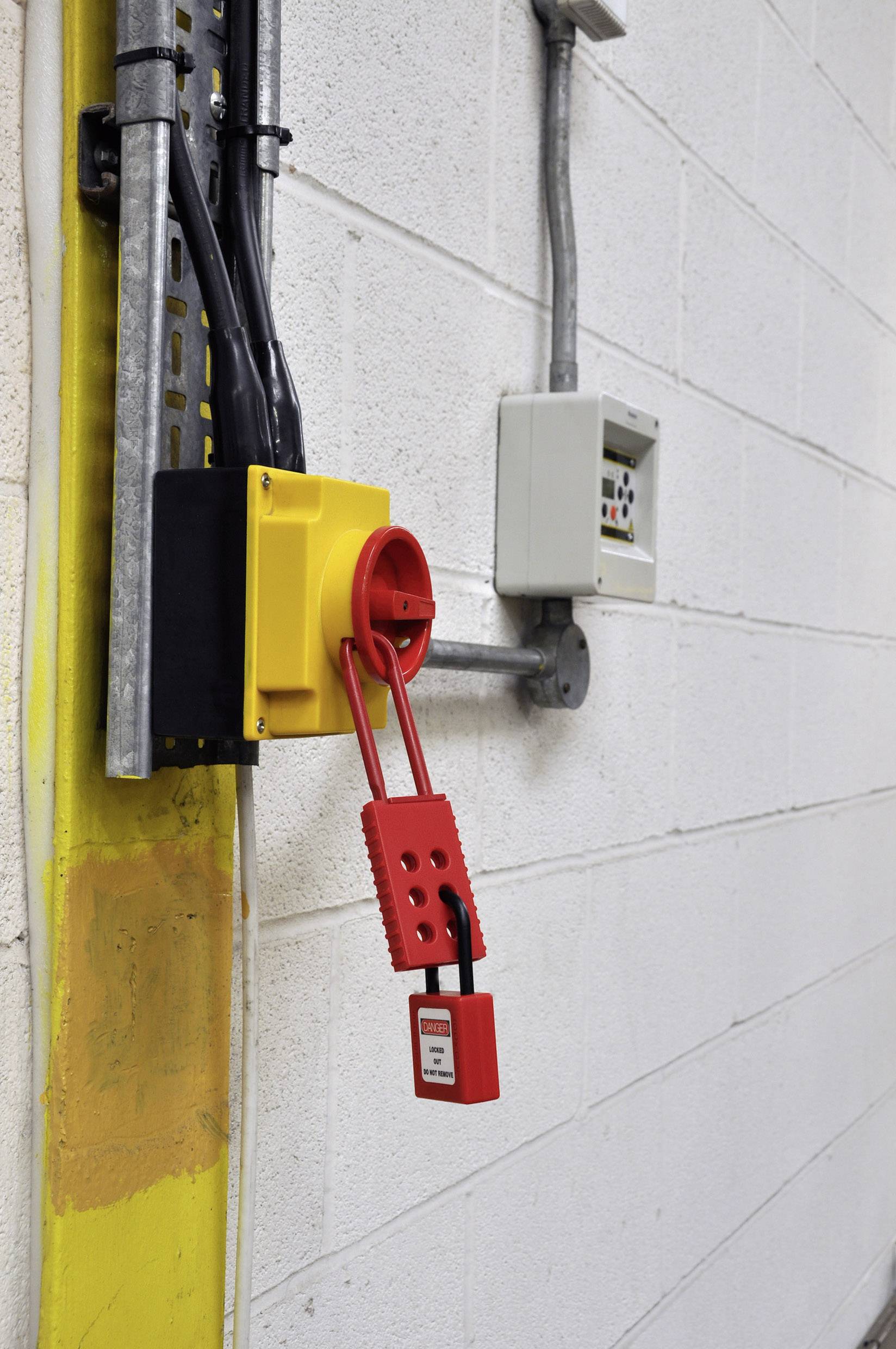 Un sistema di interruttori giallo su una parete è bloccato con un lucchetto rosso, impedendo l'accensione non autorizzata.
