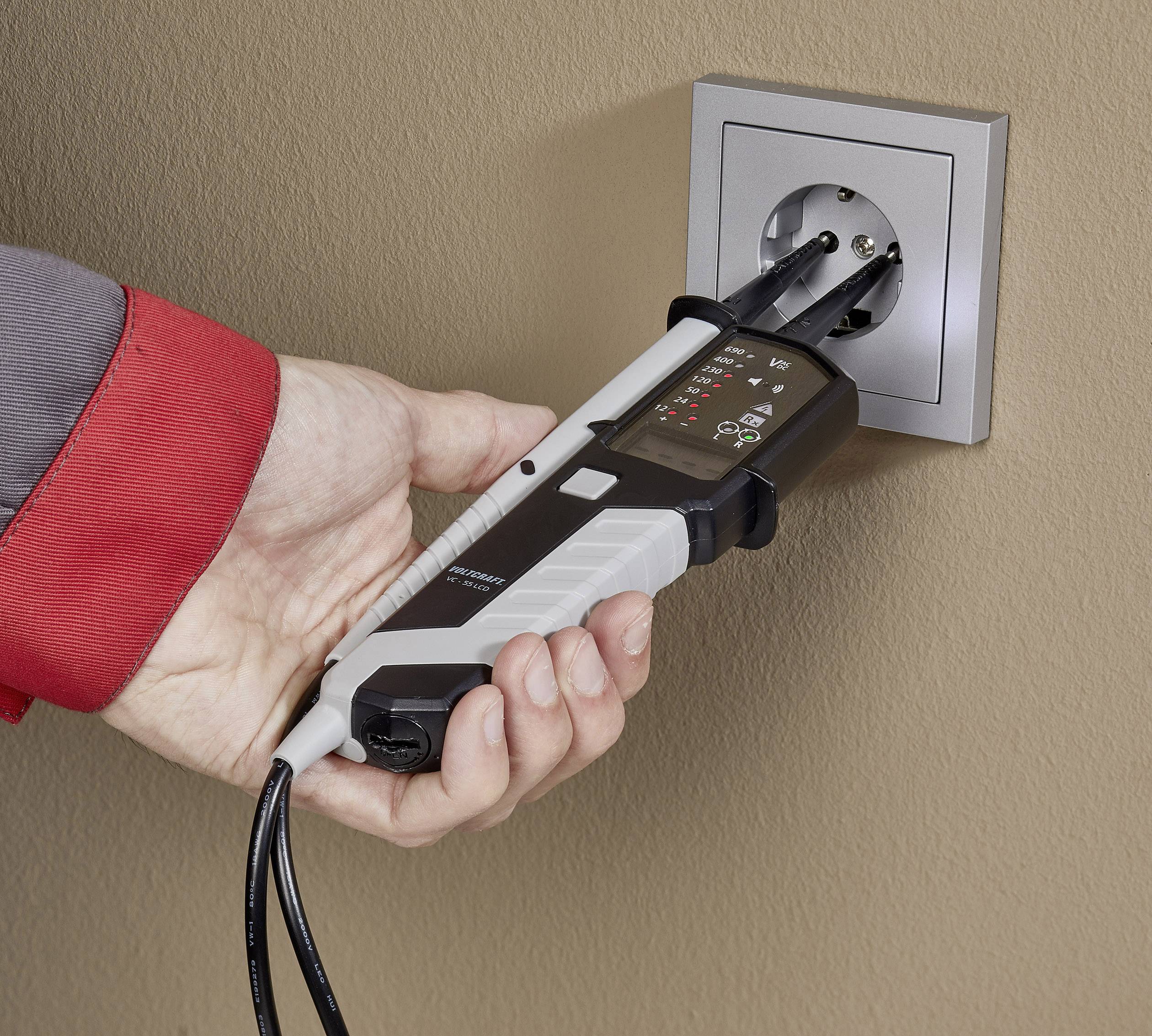 Una mano tiene un tester elettrico inserito in una presa a muro per verificare la tensione elettrica.