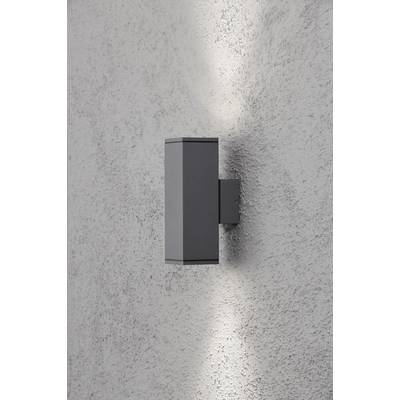 Un applique moderno grigio emana luce verso l'alto e verso il basso su una parete bianca strutturata.