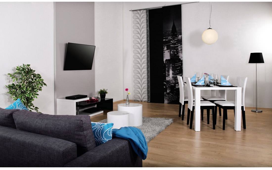 Soggiorno con divano grigio, tappeto bianco e tavolo da pranzo. Arredamento moderno con TV a parete, lampada e cuscini decorativi.