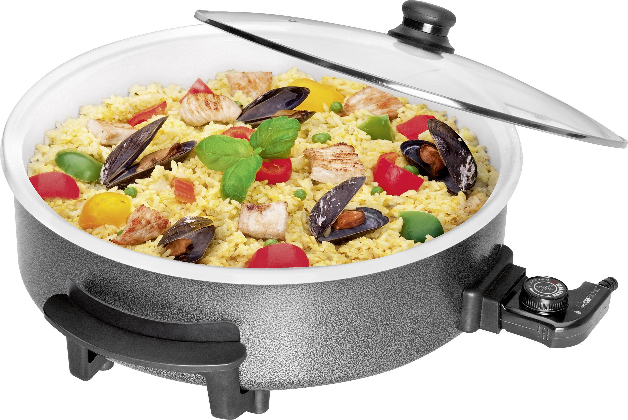 Una padella elettrica con riso giallo, conchiglie, pezzi di pollo e verdure colorate. Una foglia di basilico al centro.