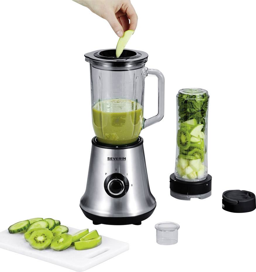 Una mano sta mettendo pezzi di mela in un frullatore a colonna argentato con un smoothie verde. Accanto: un tagliere con kiwi e un piccolo contenitore per frullare.