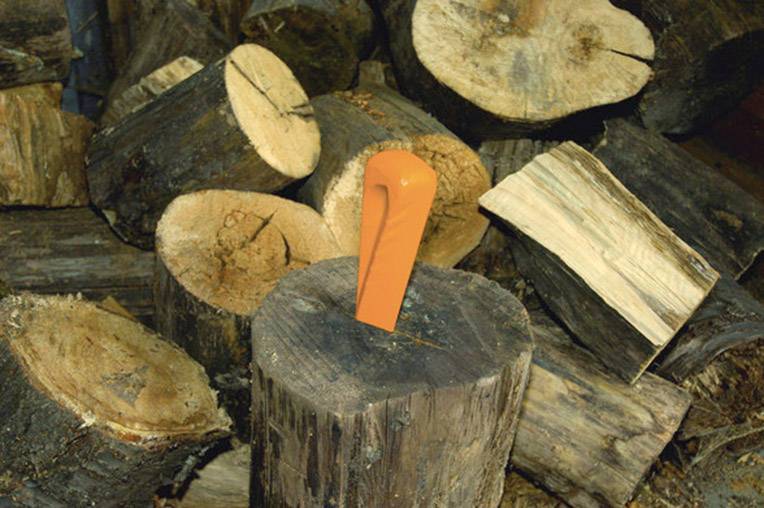 Un spaccalegna arancione è incastrato in un tronco d'albero, circondato da diverse schegge di legno tagliate.