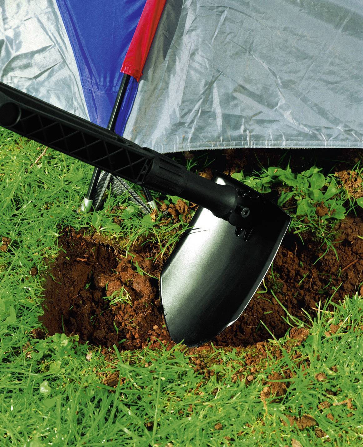 Una pala scava nel terreno accanto a una tenda su un prato.