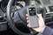 Una persona tiene in mano un dispositivo elettronico all'interno di un'auto, che potrebbe essere utilizzato per diagnosi o controlli. Sullo sfondo è visibile un volante.