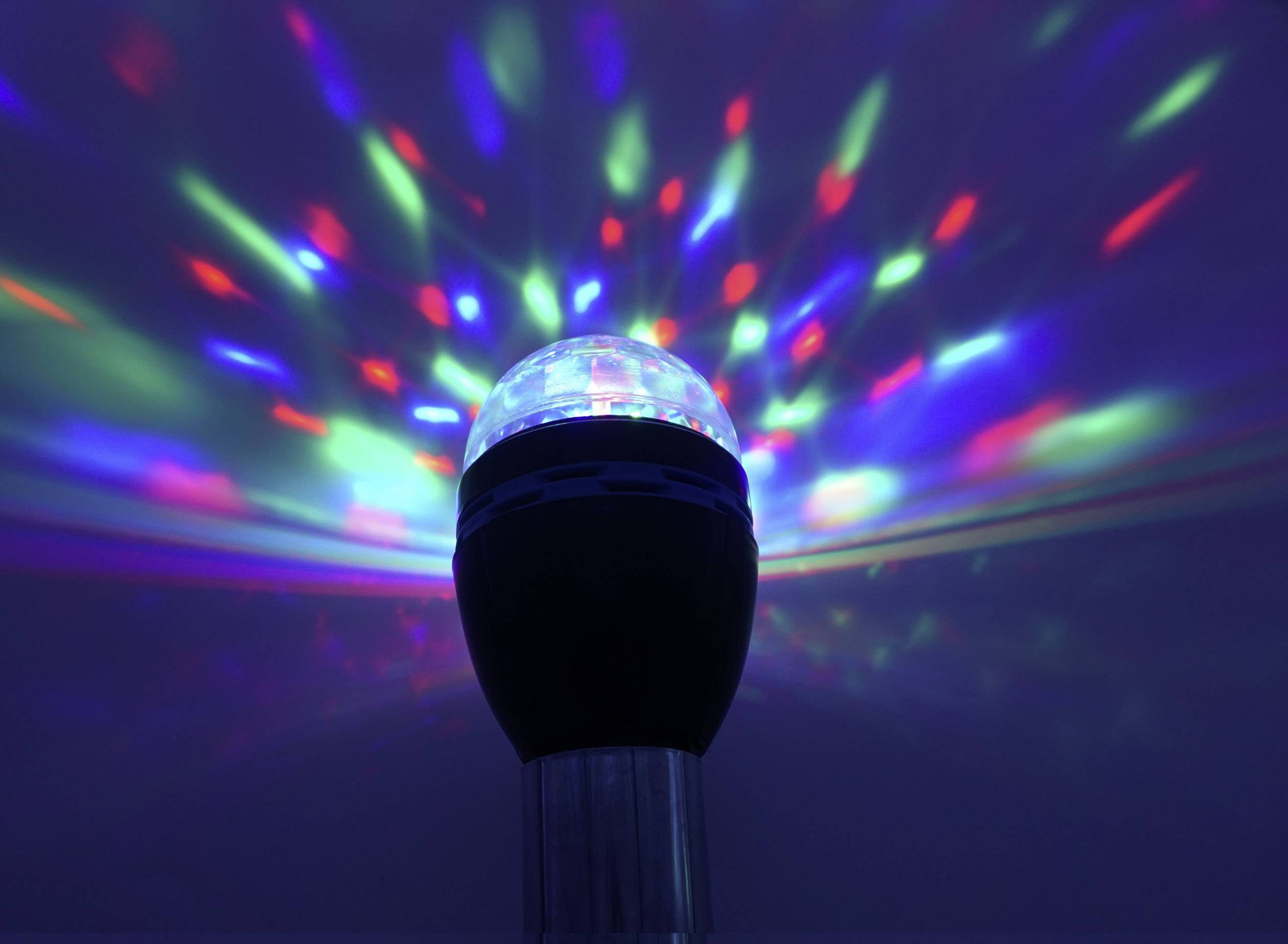 Una lampada nera proietta raggi luminosi colorati in rosso, verde e blu contro uno sfondo scuro, creando un effetto di luce.