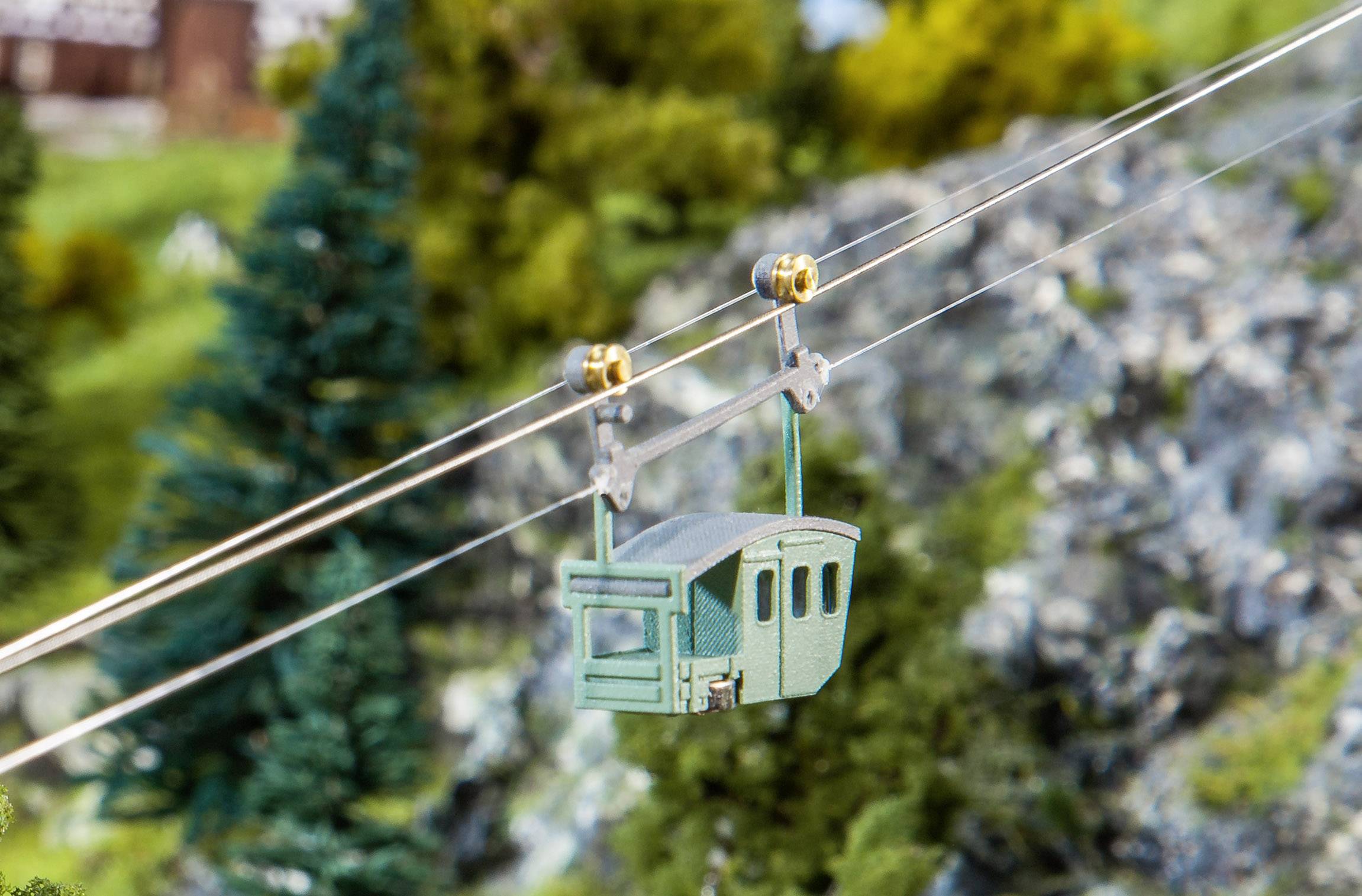 Una funivia in miniatura passa sopra un paesaggio montano modellato con alberi e rocce sullo sfondo.