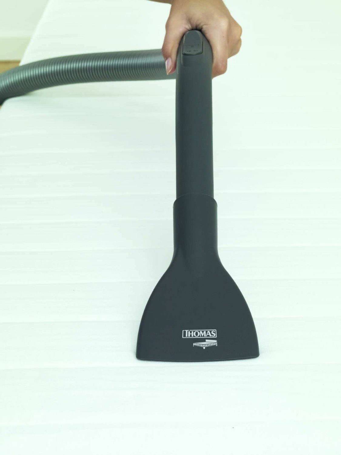 Una mano tiene un tubo dell'aspirapolvere e pulisce una superficie bianca con un ugello.