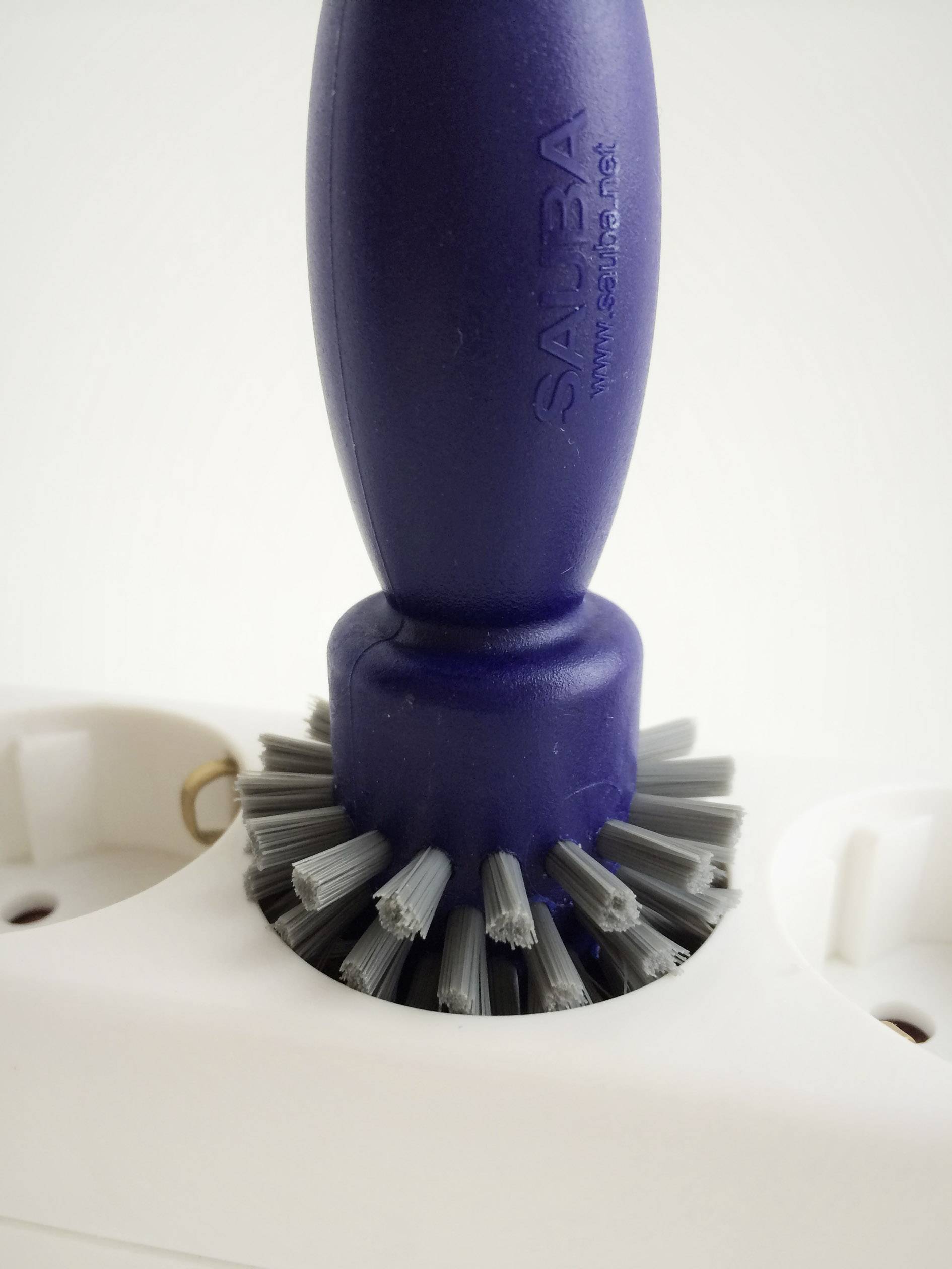 Una spazzola per la pulizia blu con setole grigie è posizionata su un involucro di plastica bianco. Nessun'altra informazione nell'immagine.