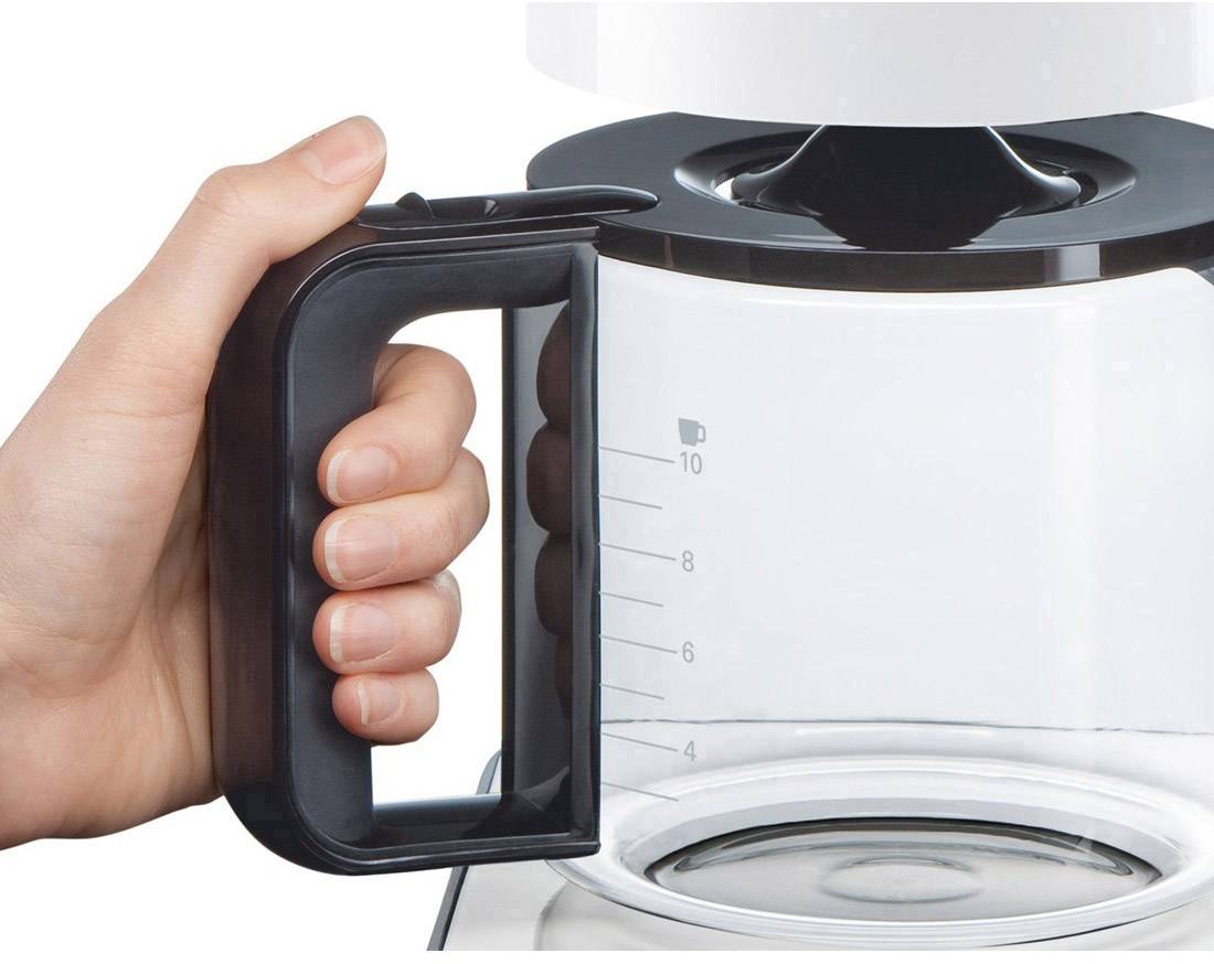 Una mano tiene l'impugnatura di una caffettiera trasparente con scala graduata, collegata a una macchina da caffè.