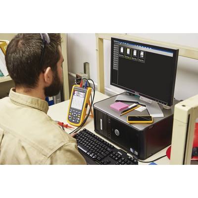 Un uomo lavora a un computer con un dispositivo di misurazione collegato che mostra i dati misurati su un monitor.