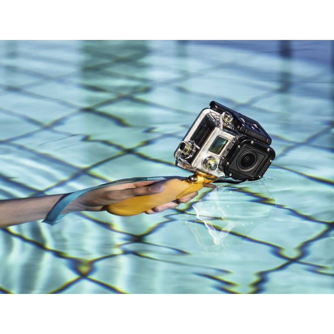 Fotocamera tenuta da un impugnatura galleggiante sull'acqua, riflette il sole, circondato da piastrelle blu in piscina.
