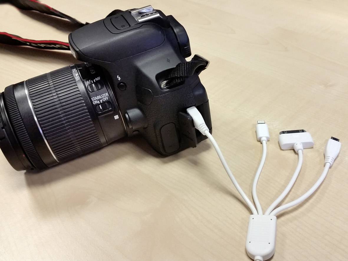 Una fotocamera digitale reflex è collegata tramite un cavo con diversi adattatori che offrono varie porte di connessione.