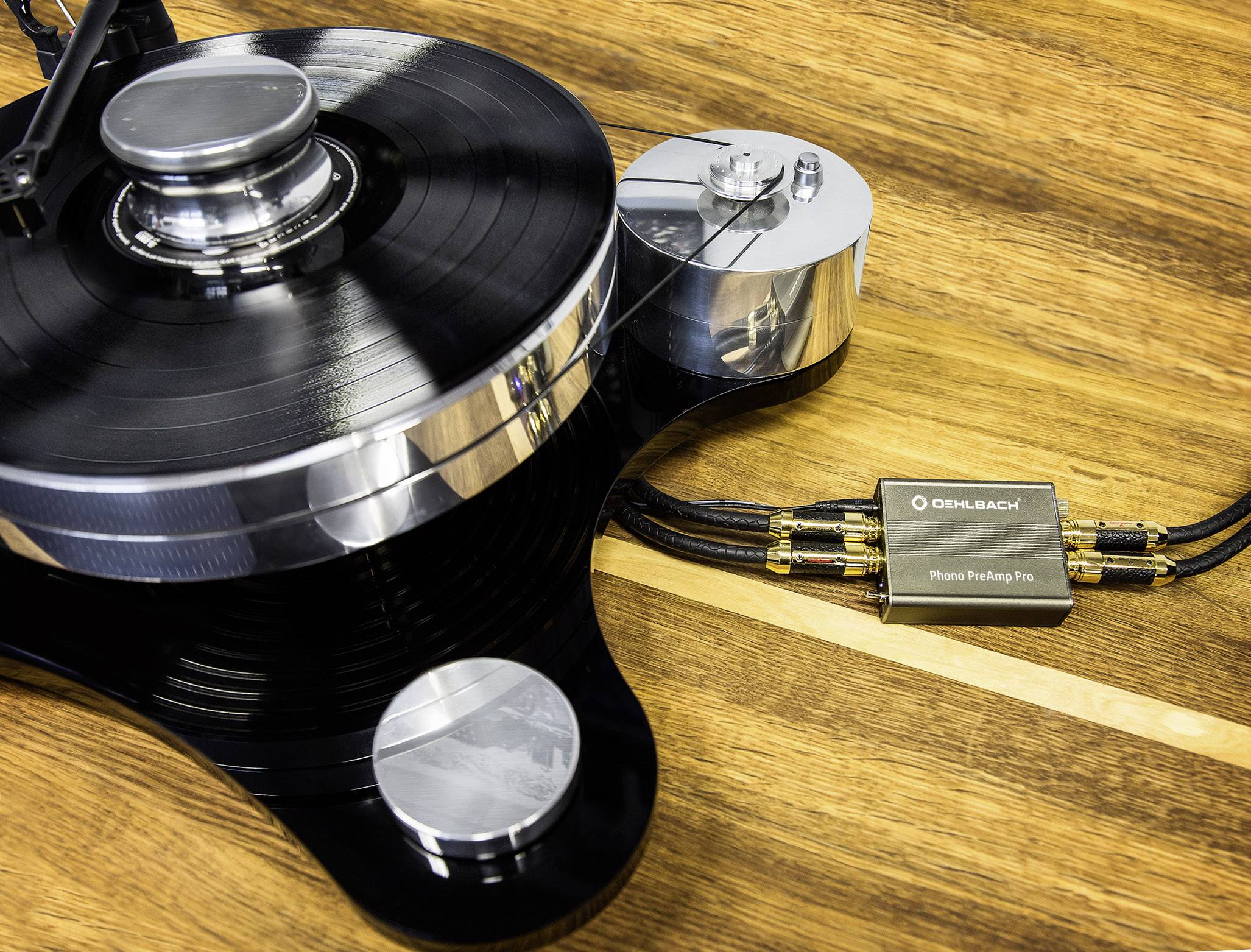 Giradischi con disco in vinile nero e cavo fonico su un tavolo di legno; superfici metalliche e opache.