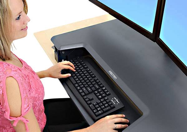 Una donna lavora in un moderno posto di lavoro con due schermi e una tastiera integrata su una scrivania nera.