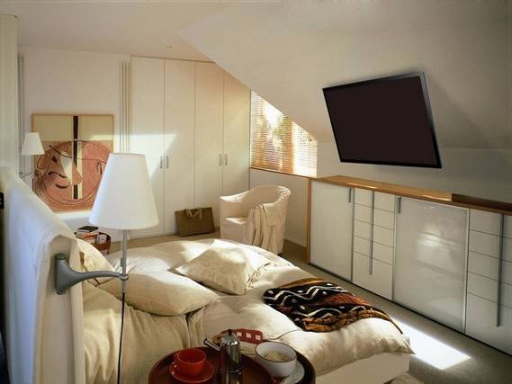 Una camera da letto accogliente con un grande letto matrimoniale, una poltrona, una televisione a schermo piatto appesa alla parete e una finestra con veneziane.