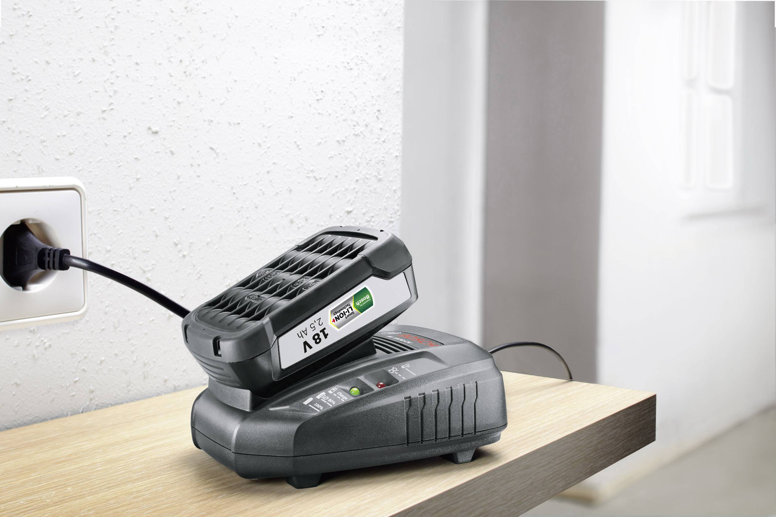 Una batteria viene caricata in un caricabatterie a parete. Sulla batteria è riportato 'Li-ion 28V'. Il dispositivo mostra uno stato di carica verde.