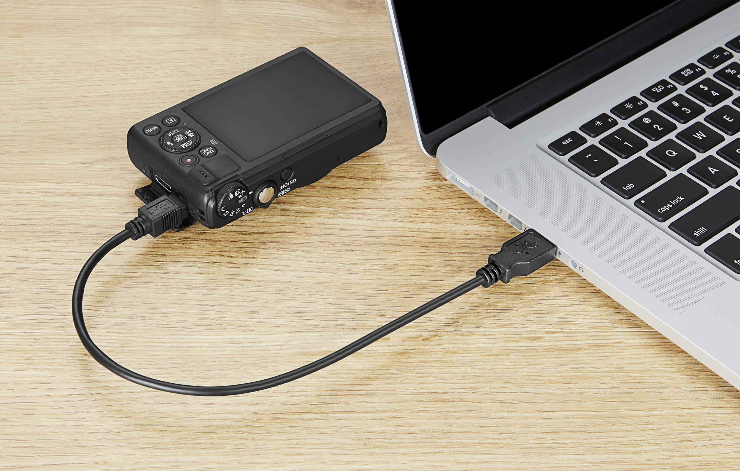 'Una fotocamera digitale è collegata a un laptop tramite un cavo USB. Il laptop mostra una tastiera parzialmente aperta.'