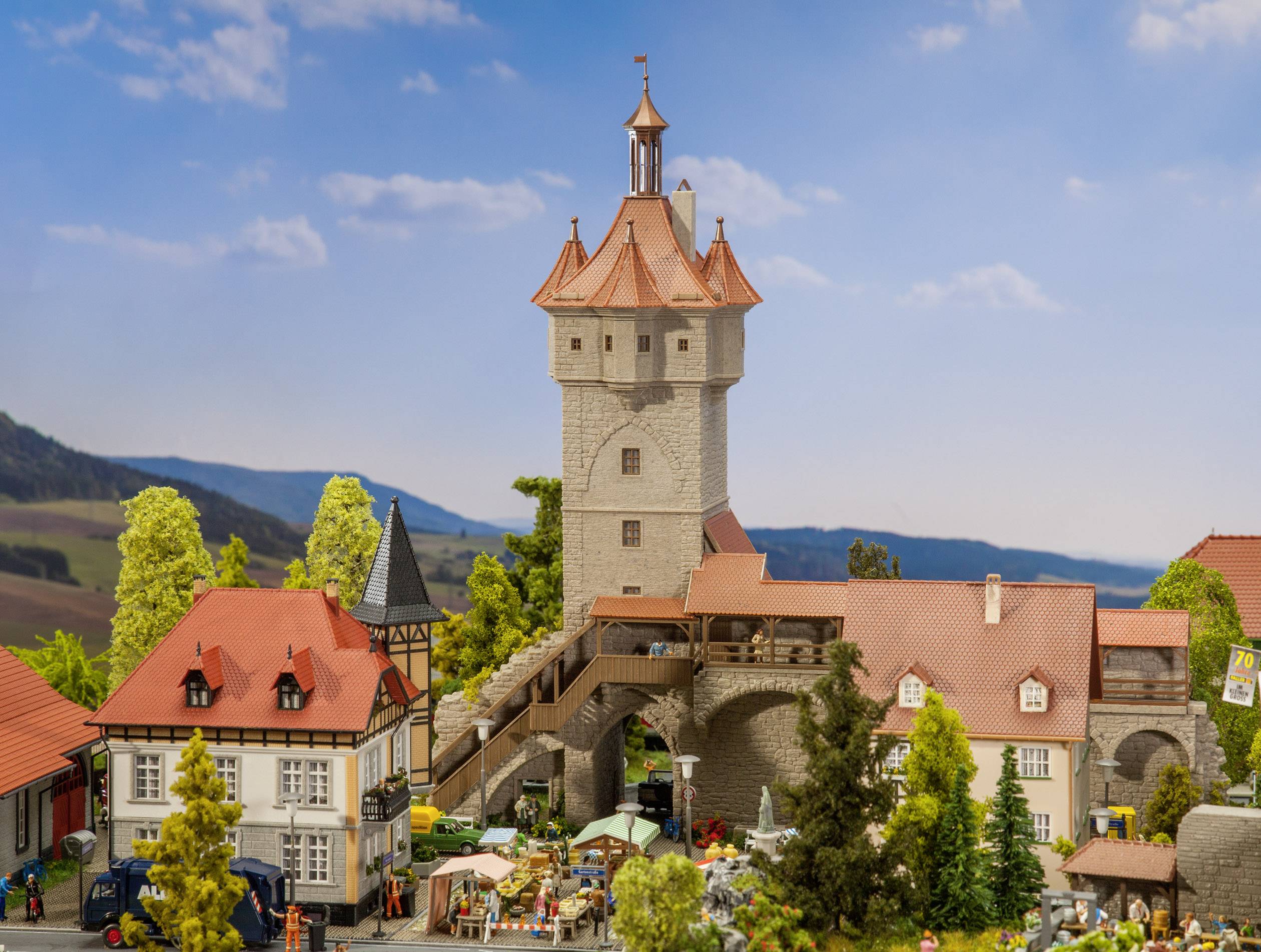 Un modellino in miniatura mostra una città medievale con un'alta torre, circondato da case a graticcio e persone che si muovono in un mercato.