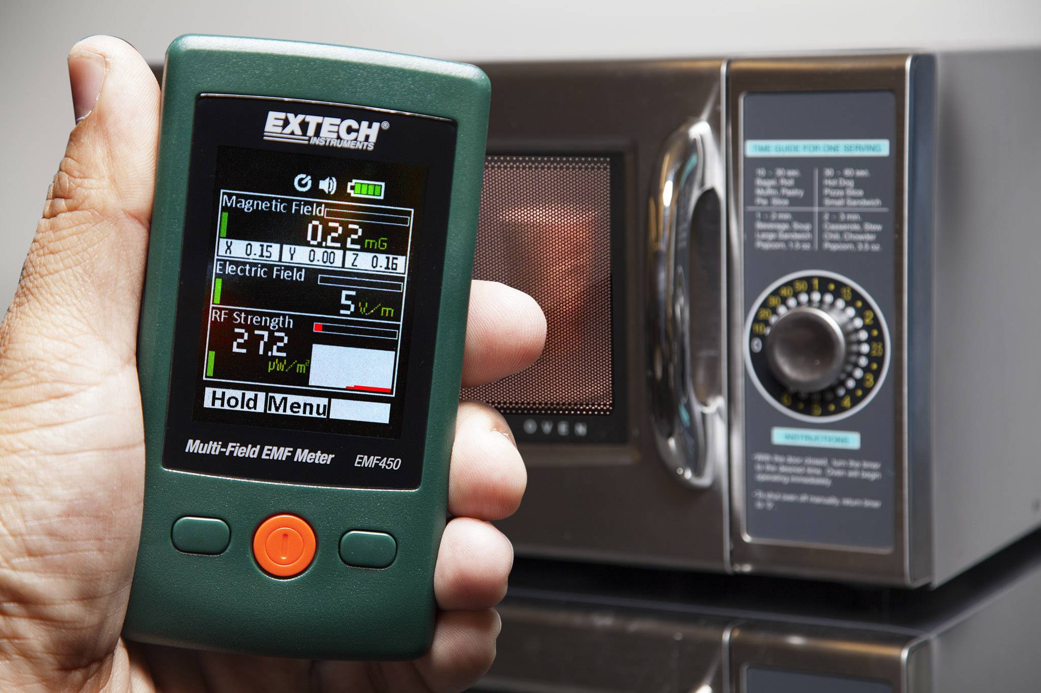 Una persona tiene un dispositivo di misurazione EMF di fronte a un forno a microonde. Lo strumento mostra i valori dei campi elettrici e magnetici.