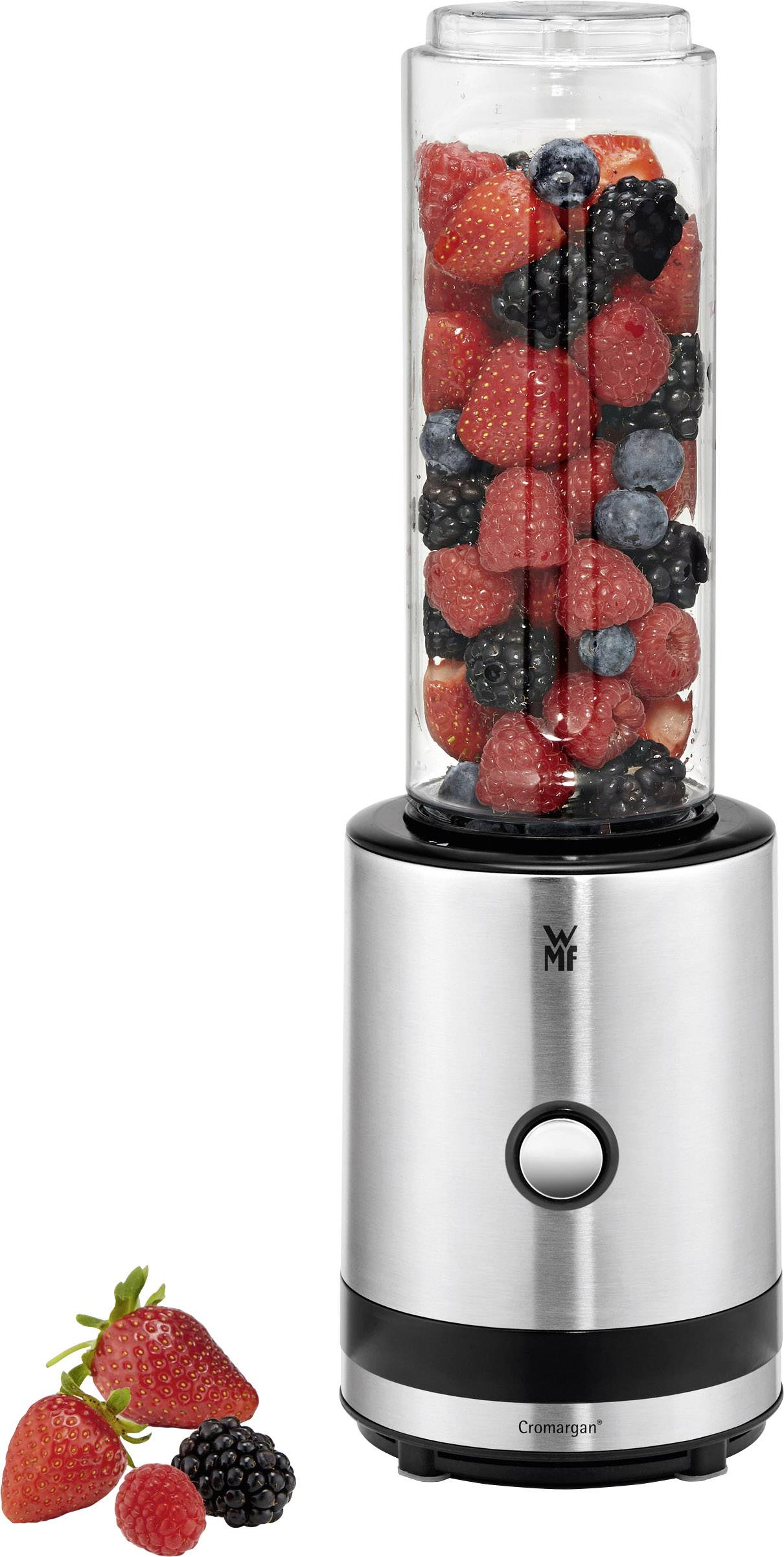 Un frullatore argentato con caraffa trasparente, riempito con fragole, lamponi, more e mirtilli. Accanto sono sparse alcune bacche.