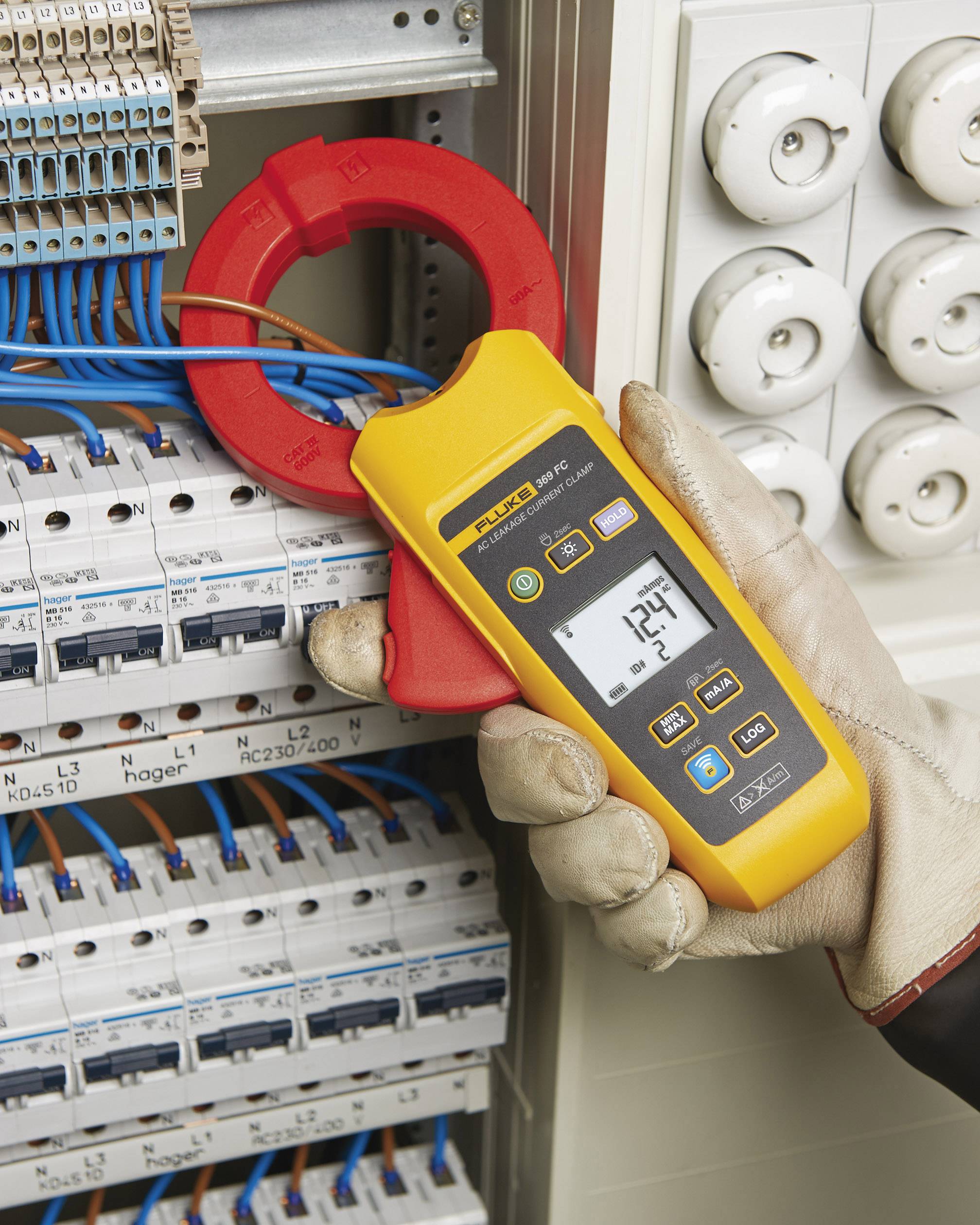 Una persona con guanti da lavoro utilizza un multimetro giallo per misurare il flusso di corrente in un quadro elettrico.