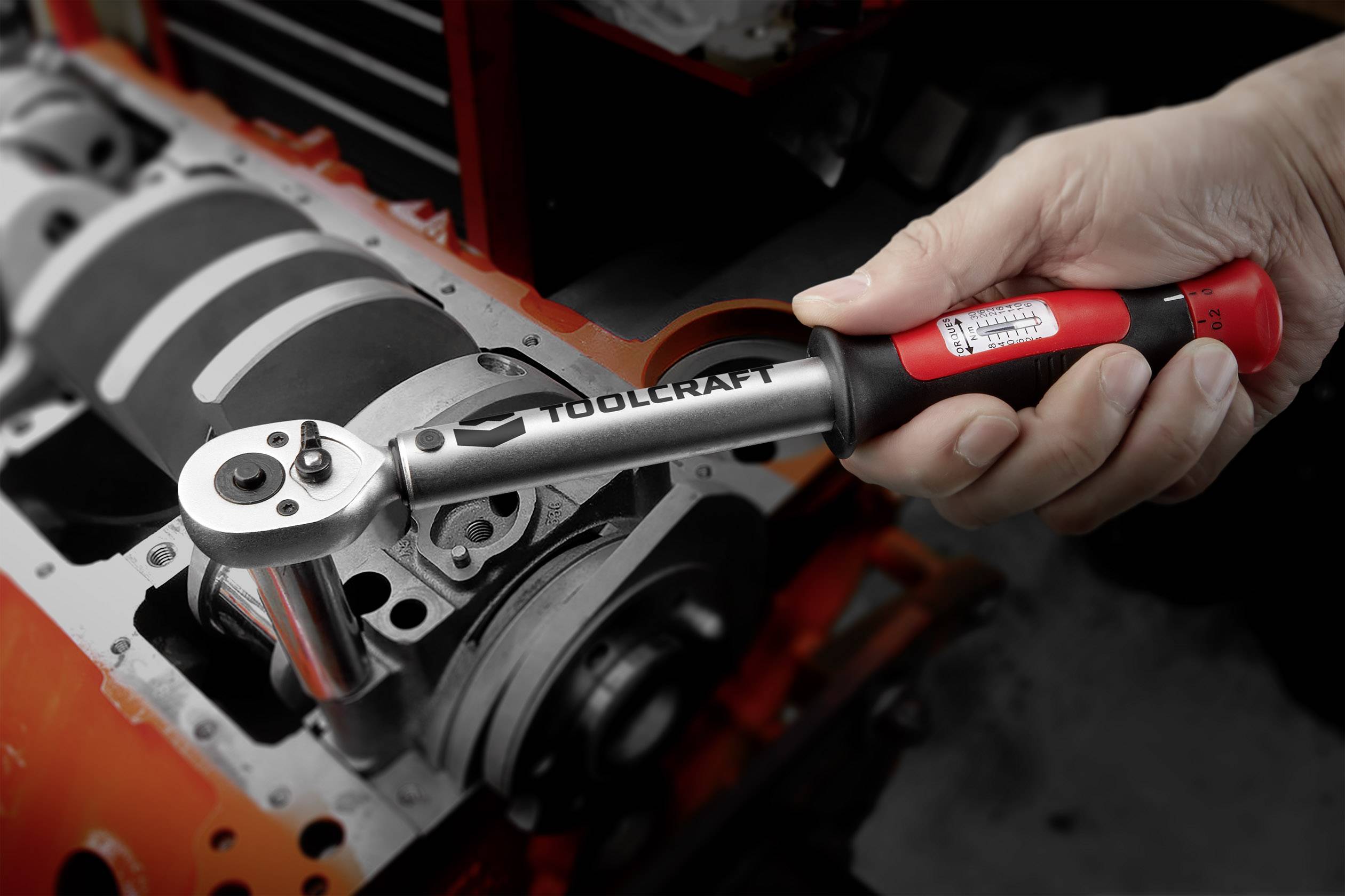 Una mano tiene una chiave dinamometrica Toolcraft che viene applicata a un componente motore o macchina.