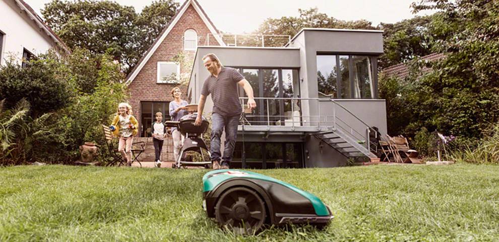 Una famiglia osserva un rasaerba automatico mentre si trova nel giardino di una casa moderna.