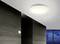 Lampadario rotondo bianco in una stanza moderna con pareti scure e una finestra che mostra un crepuscolo blu scuro.