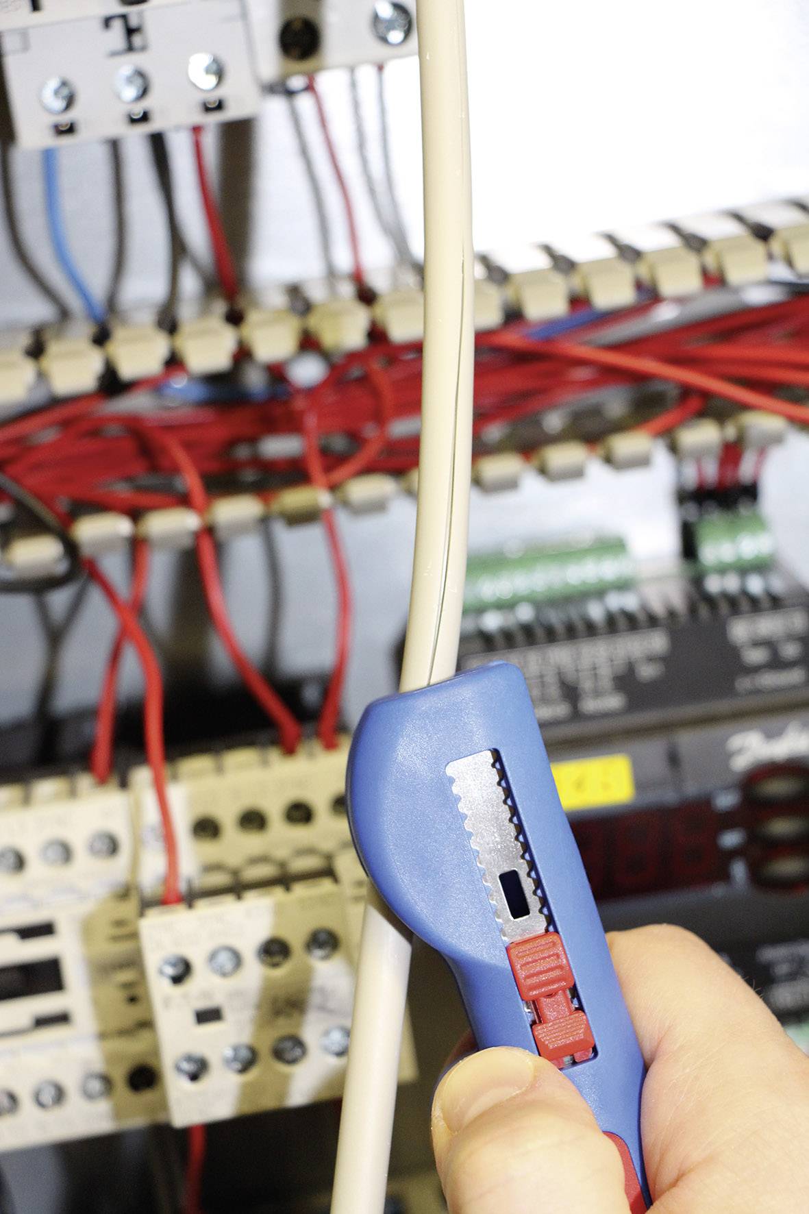 Una mano tiene un spelacavi e rimuove l'isolamento da un cavo. Sullo sfondo sono visibili circuiti elettrici.