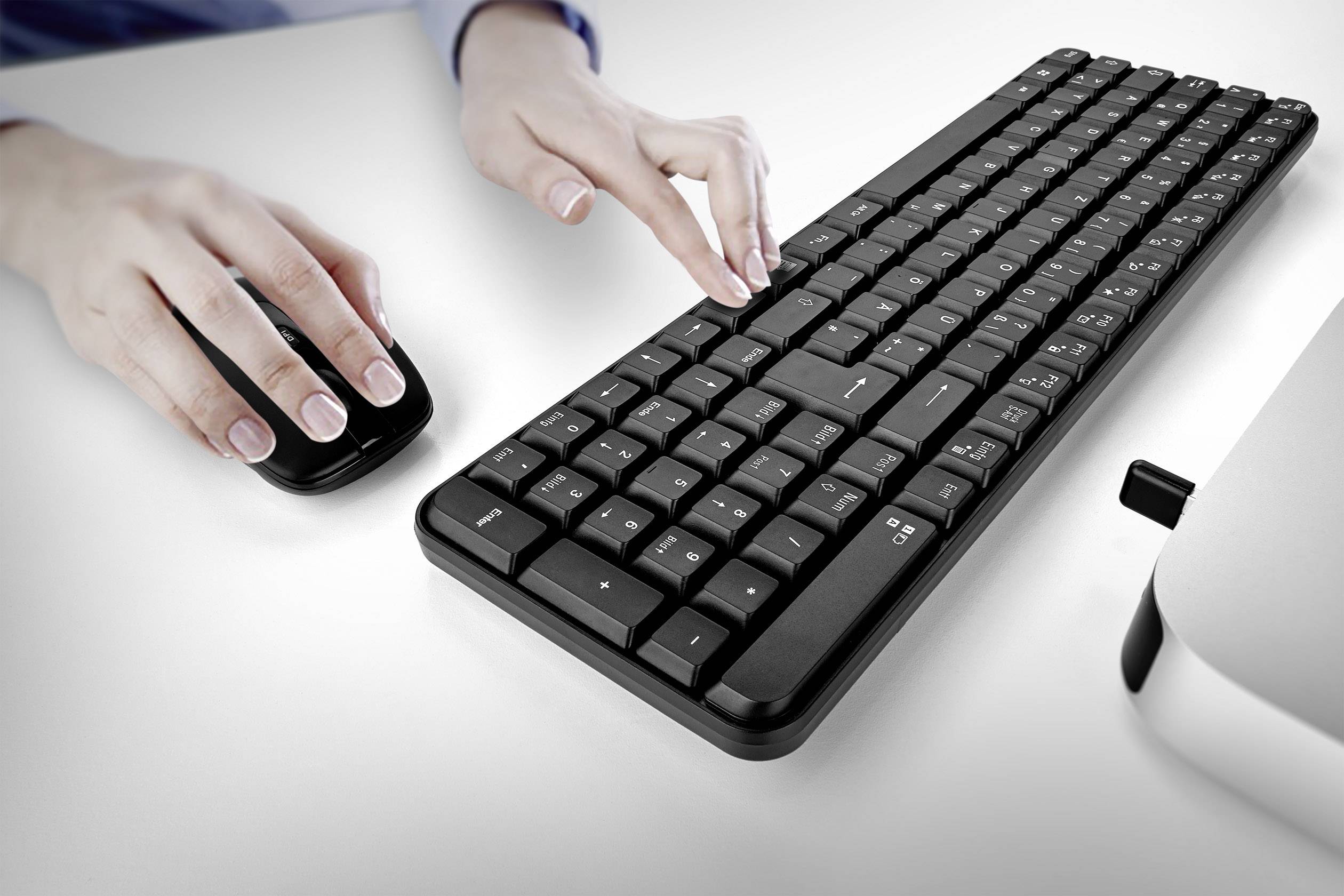 Mani che utilizzano una tastiera e un mouse su una scrivania bianca, simboleggiando il lavoro al computer o attività online.