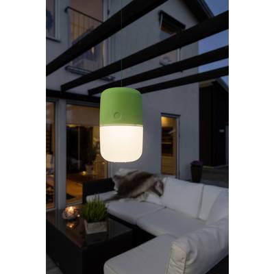 Una lampada verde è appesa sopra un divano bianco in una terrazza moderna al crepuscolo. Sullo sfondo si vedono grandi finestre e una casa.