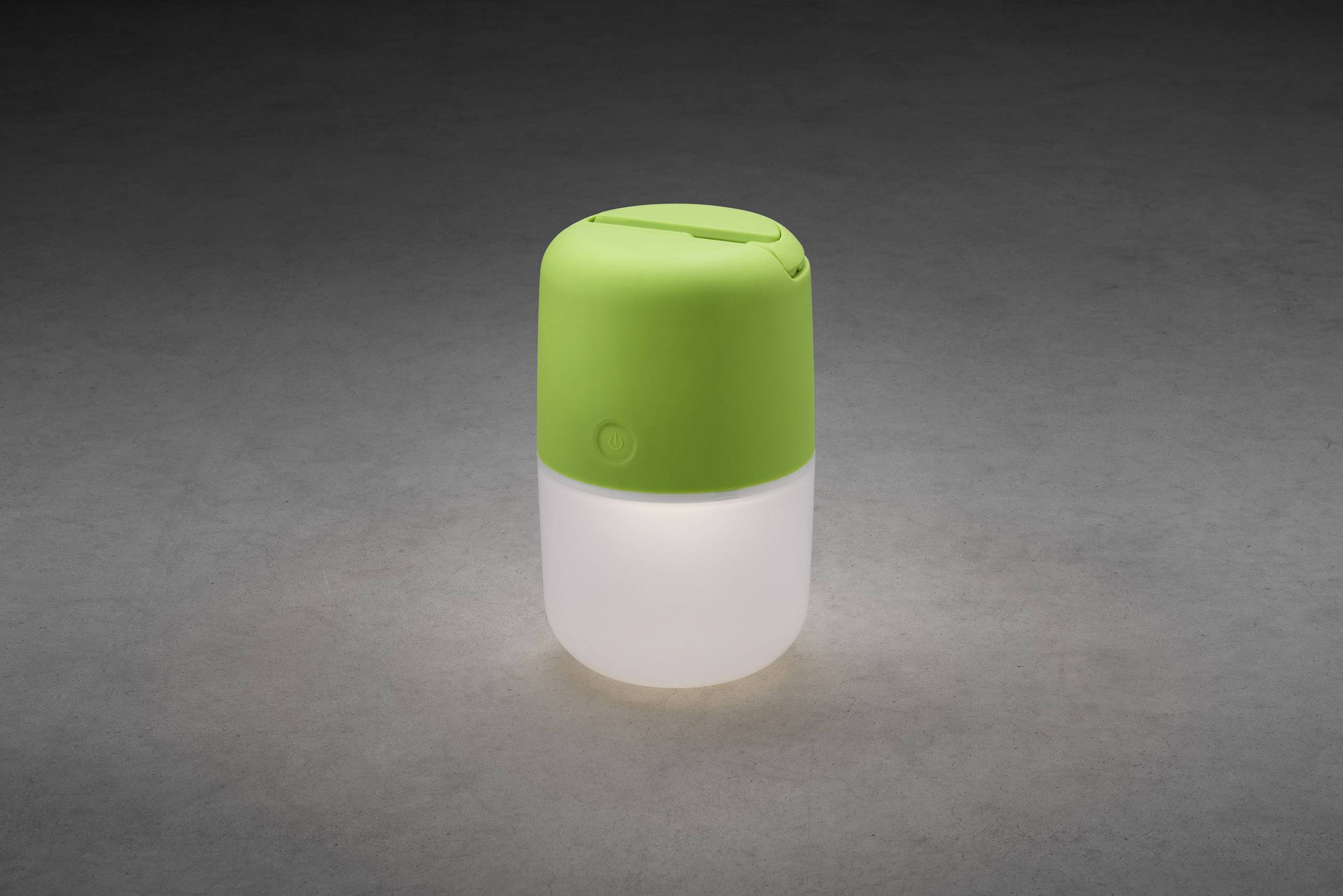 Un luce notturna a LED verde su sfondo grigio, composto da un coperchio verde con interruttore rotondo e un corpo luminoso bianco.