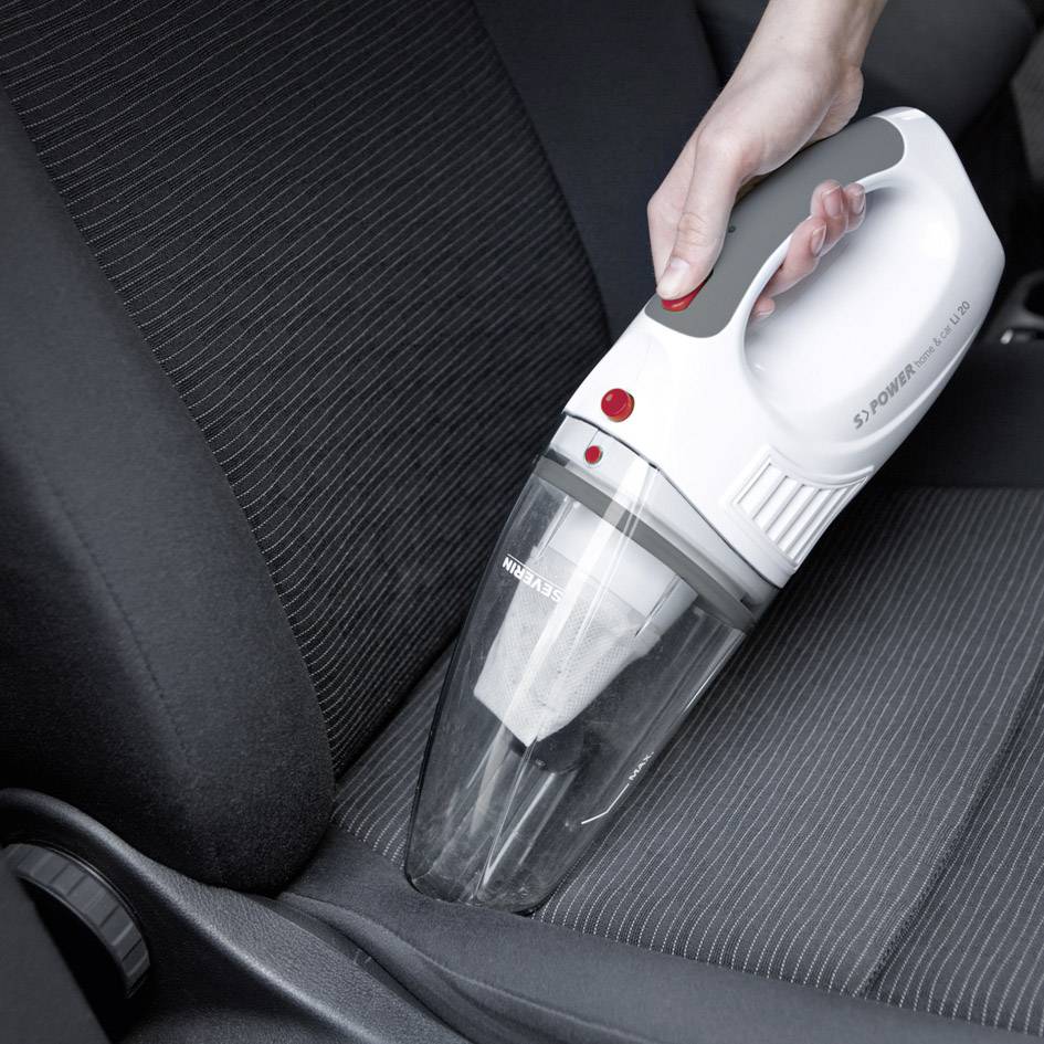 Una persona sta utilizzando un aspirapolvere portatile per pulire il sedile di un'auto. L'aspirapolvere è bianco con dettagli grigi.