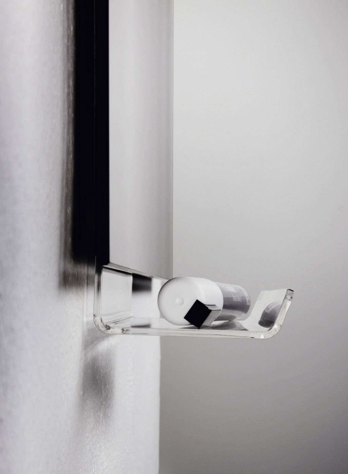 Una mensola minimalista al muro sostiene un piccolo contenitore rotondo bianco accanto a un piccolo cubo nero.