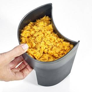 Una mano tiene un contenitore metallico riempito di ingredienti tritati di un arancione brillante.