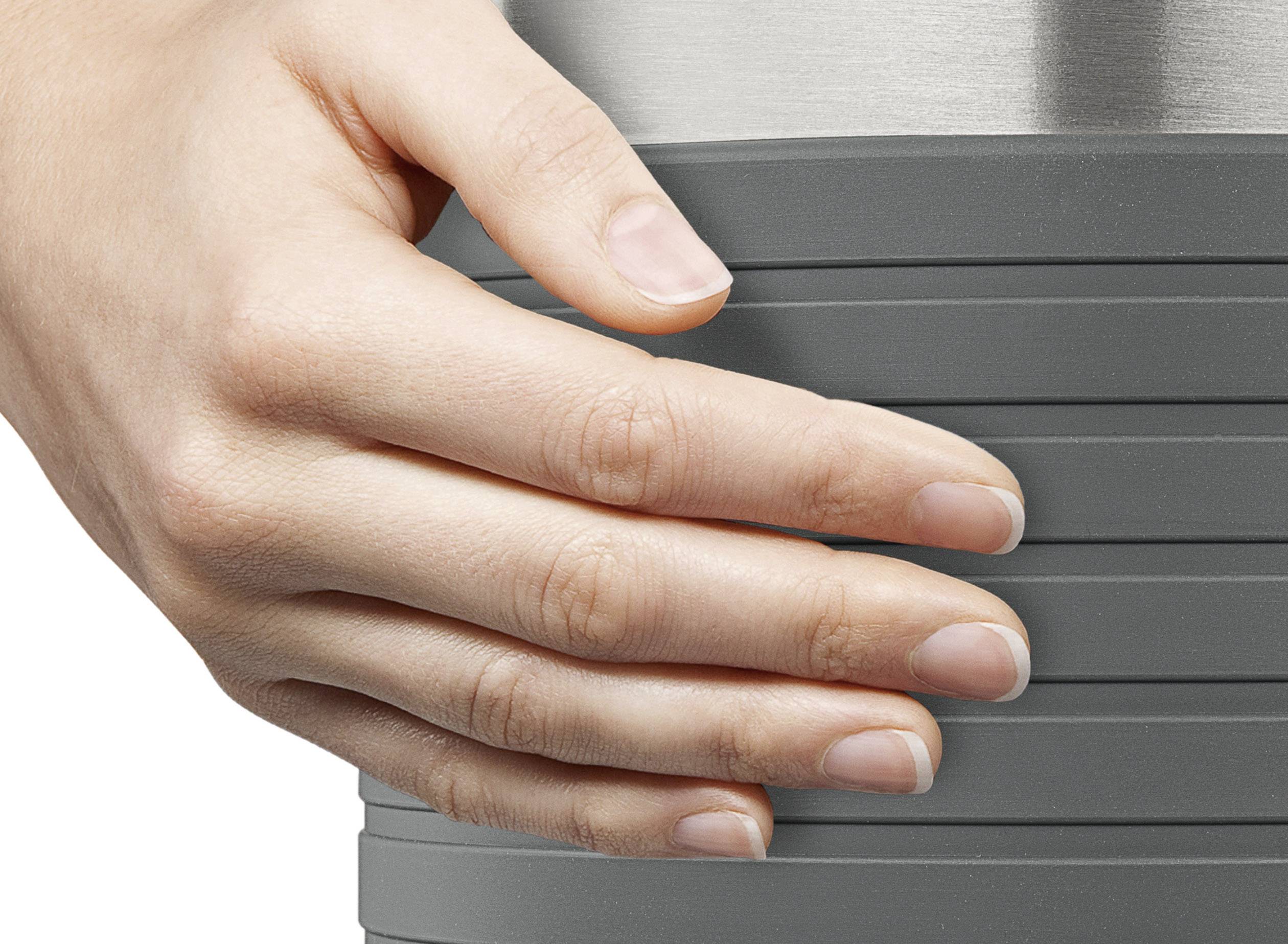 Una mano tiene una tazza grigia con scanalature. La mano è posizionata rilassata attorno alla tazza, a indicare comfort o stabilità.