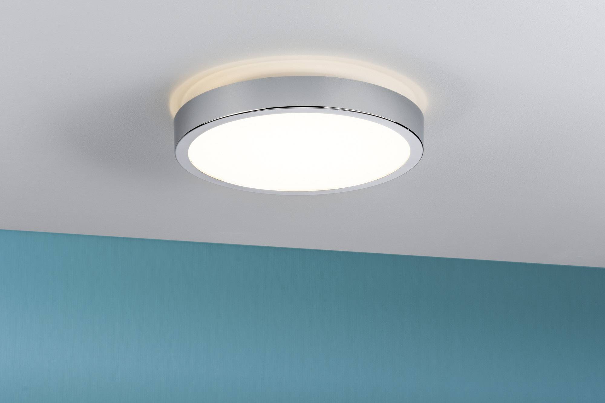 Un'elegante plafoniera LED rotonda con cornice argentata illumina un soffitto bianco. Sotto di essa è visibile una parete color turchese.