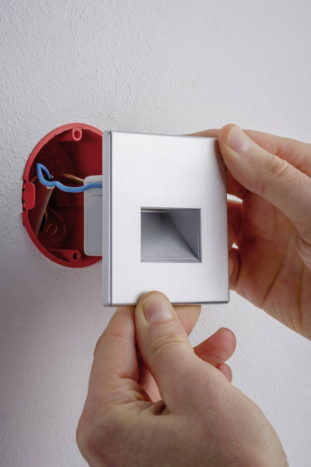 Una persona sta installando un coperchio di protezione su una presa elettrica esposta con fili blu nella parete.