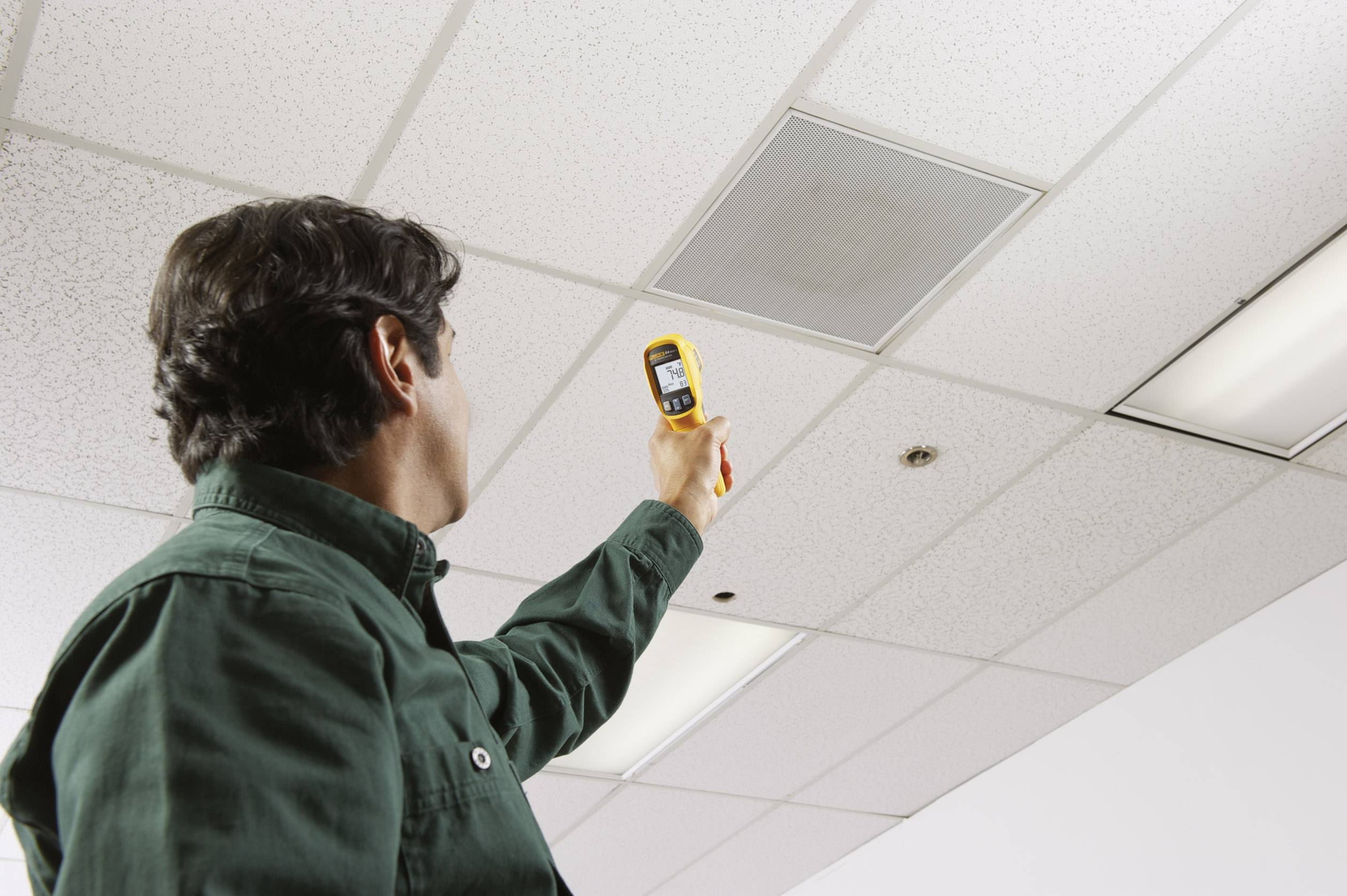 Un uomo misura la temperatura di una superficie del soffitto con un termometro a infrarossi in un edificio per uffici.