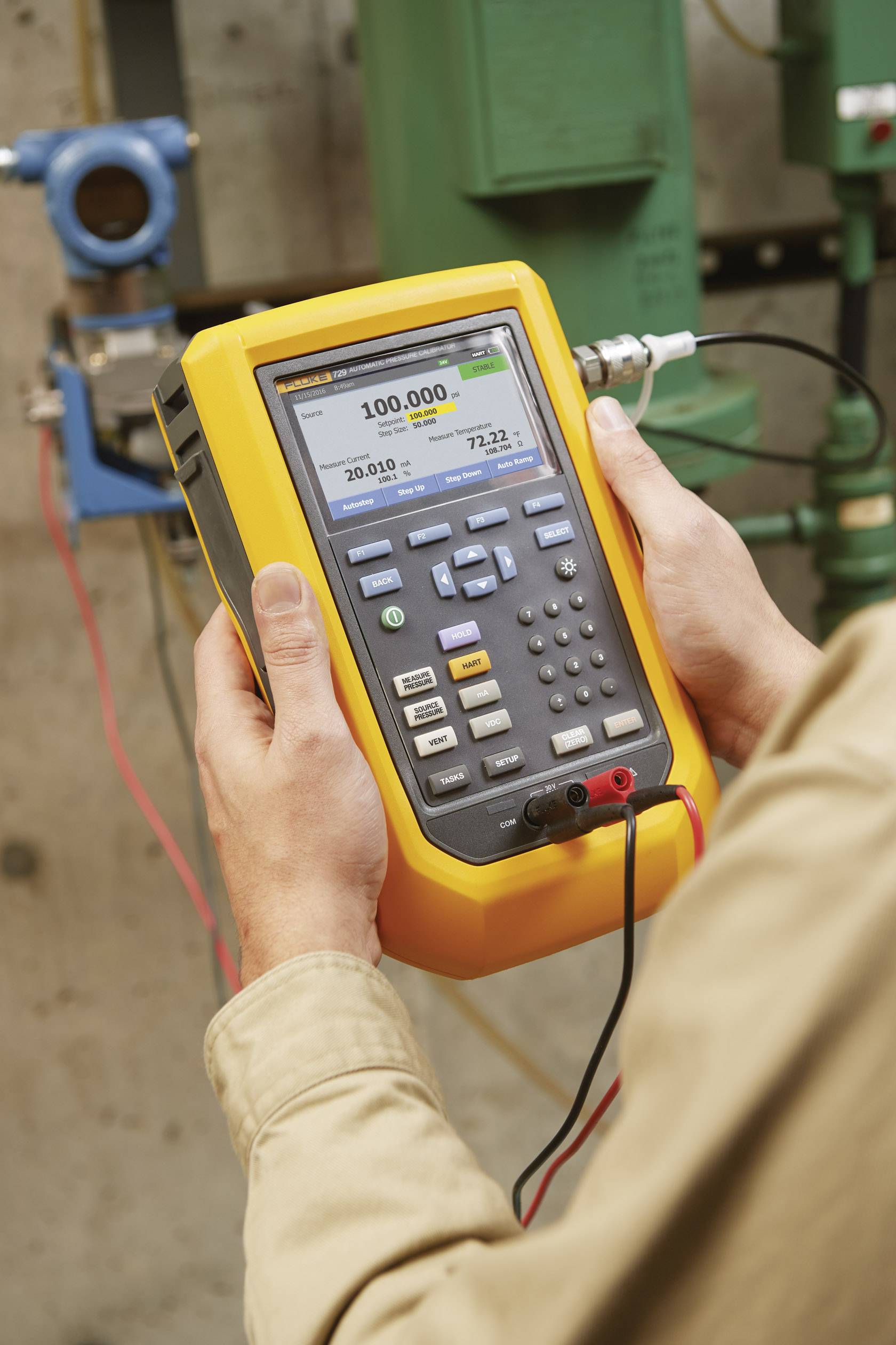 Una persona tiene in mano uno strumento portatile di misurazione per la calibrazione della pressione, con visualizzazione dei valori di pressione e connessioni elettriche sullo sfondo.
